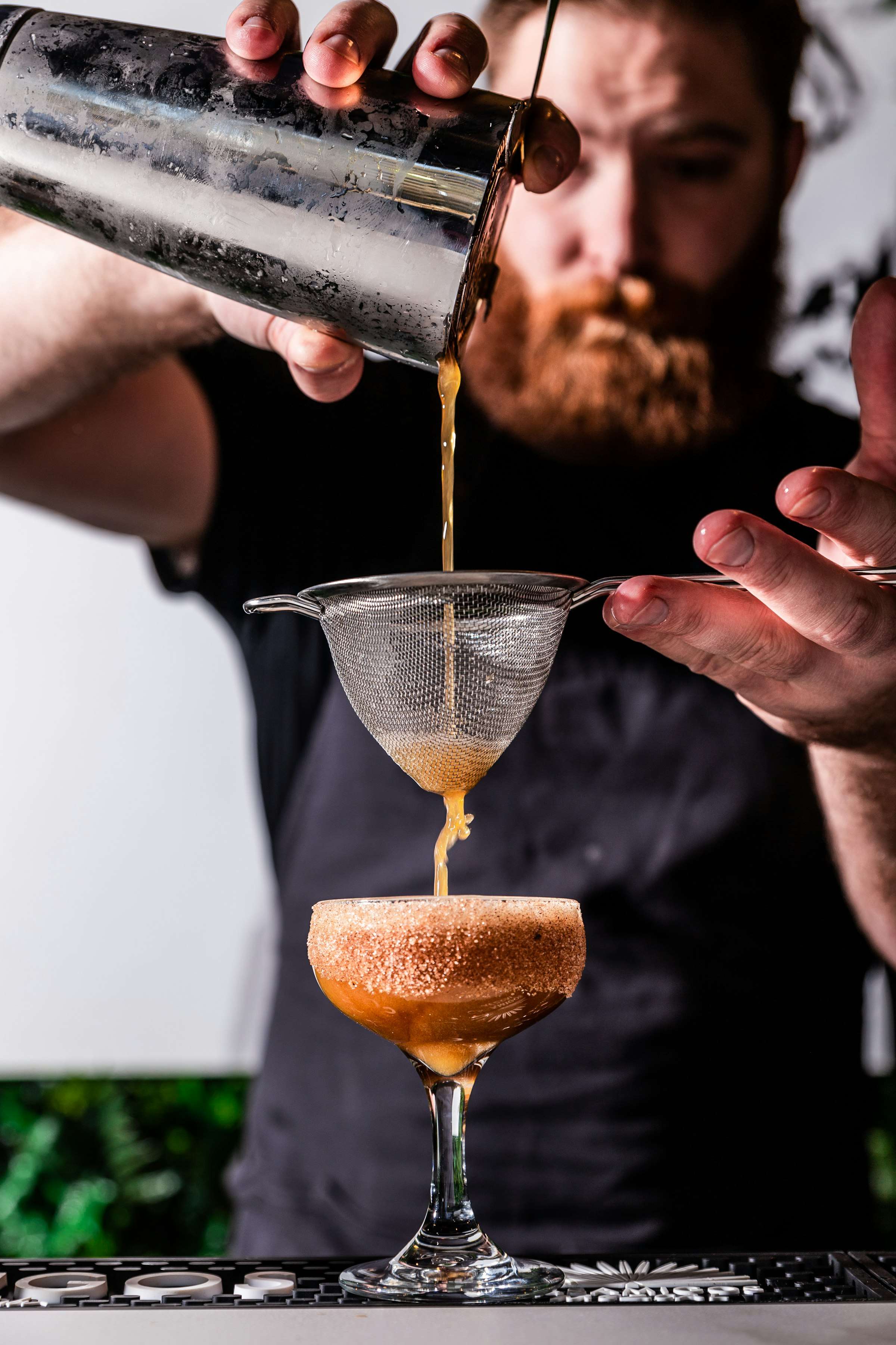Cocktail wird durch ein Barsieb ins Glas abgeseiht
