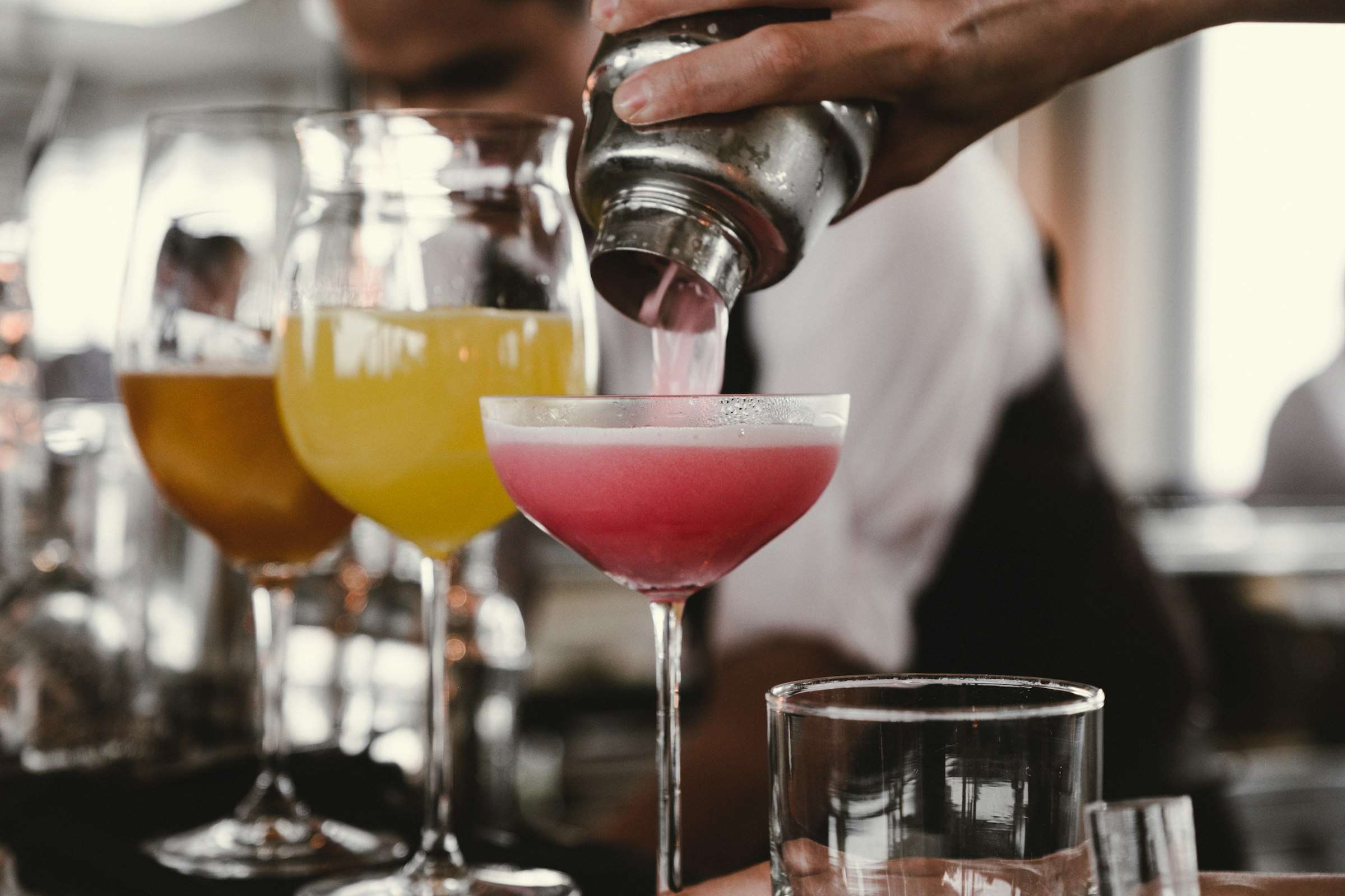 Cocktail wird aus dem Shaker in Gläser gegossen