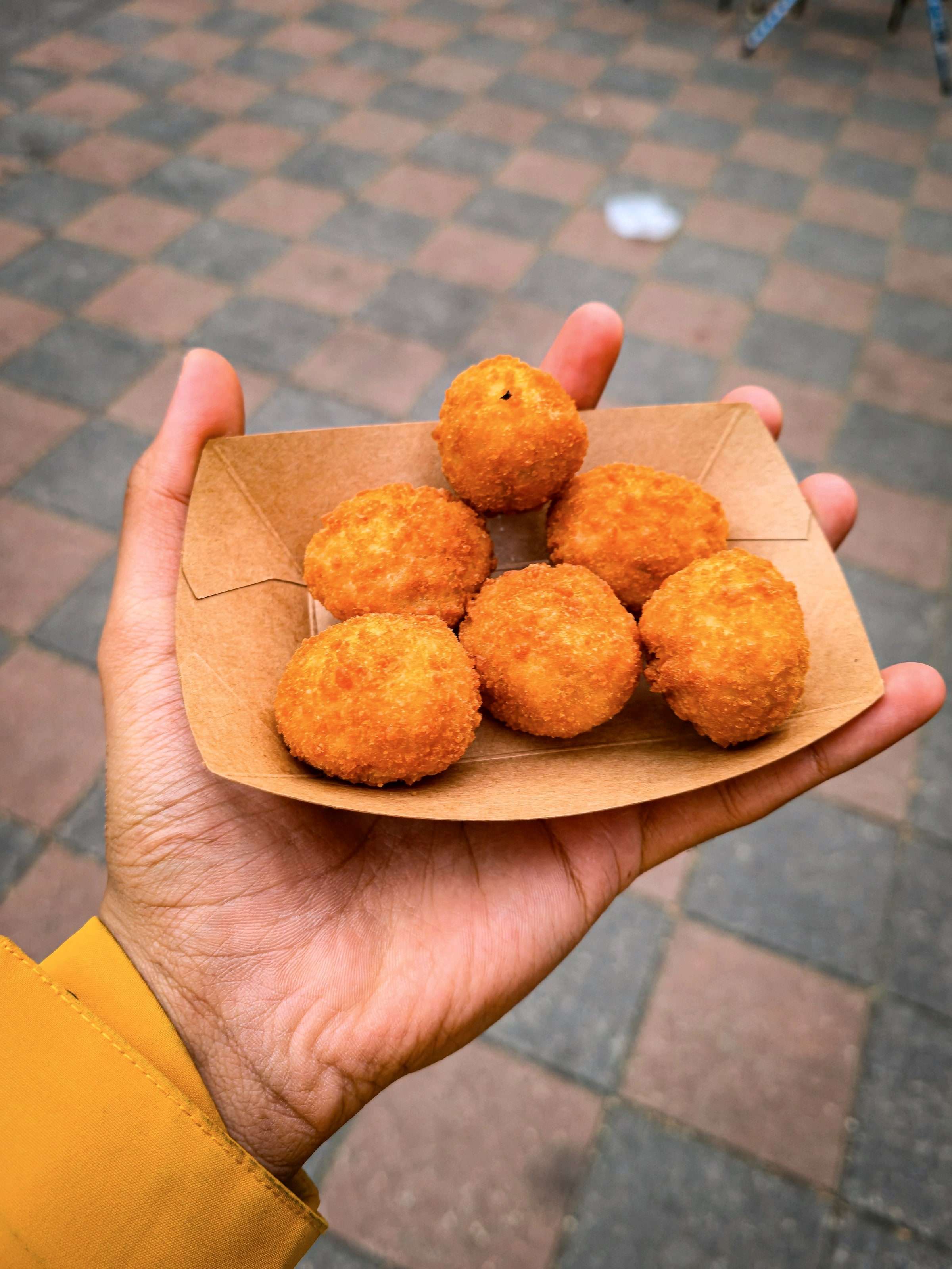 Hand hält ein Papierschälchen mit frittiertem Fingerfood